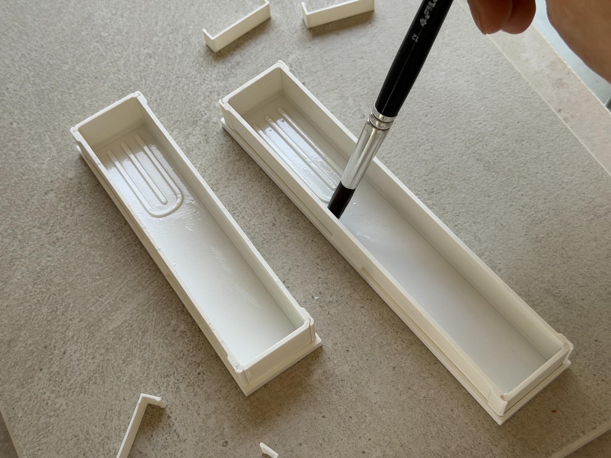 A brush applying a thin coat of release oil inside two white 3D-printed molds