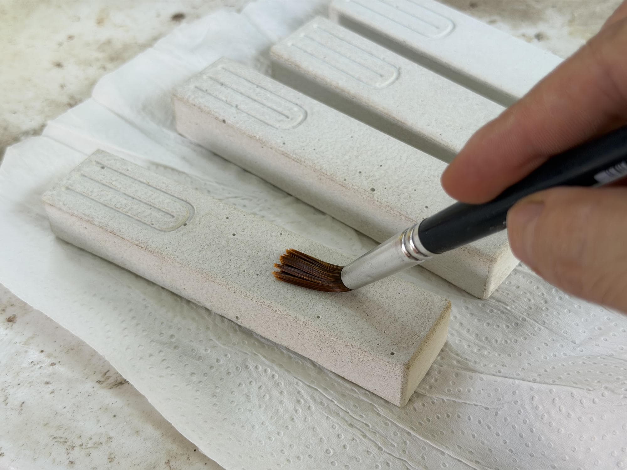 A small brush applying sealer to several finished concrete mezuzah cases