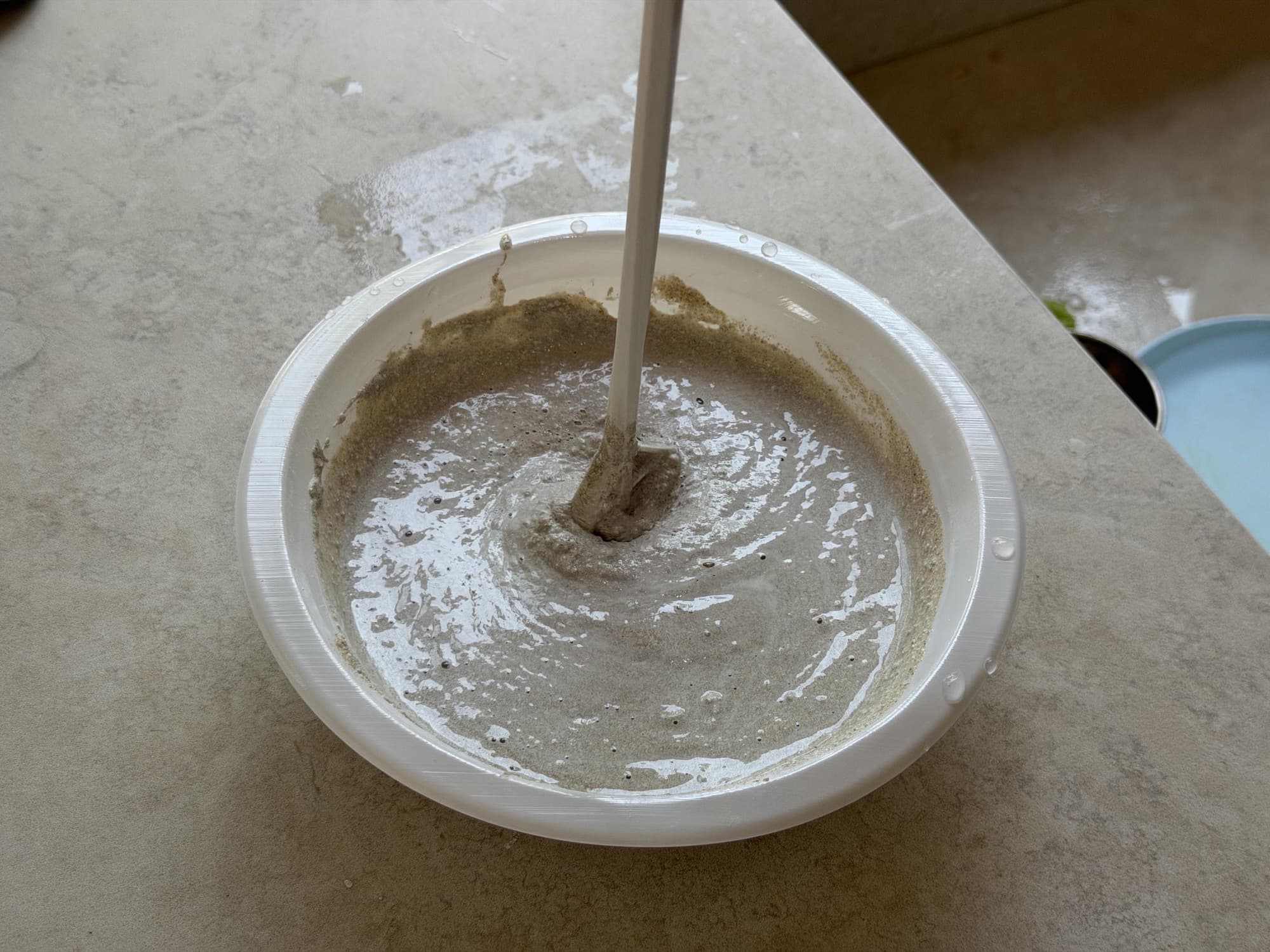 Wet concrete being mixed in a shallow plastic bowl with a drill-powered paddle